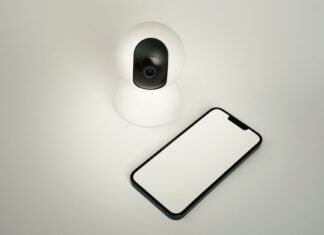 Jak wykorzystać sztuczną inteligencję i Internet Rzeczy do poprawy bezpieczeństwa w inteligentnym domu Kamera bezpieczeństwa smart home obok smartfona na białym tle