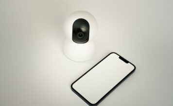 Kamera bezpieczeństwa smart home obok smartfona na białym tle