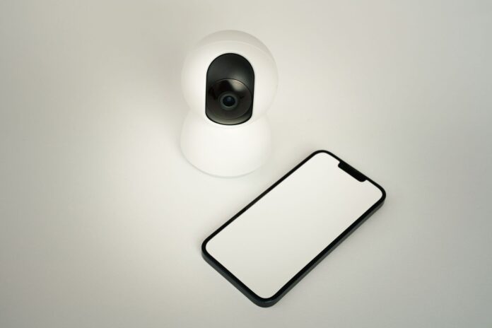 Kamera bezpieczeństwa smart home obok smartfona na białym tle Kamera bezpieczeństwa smart home obok smartfona na białym tle