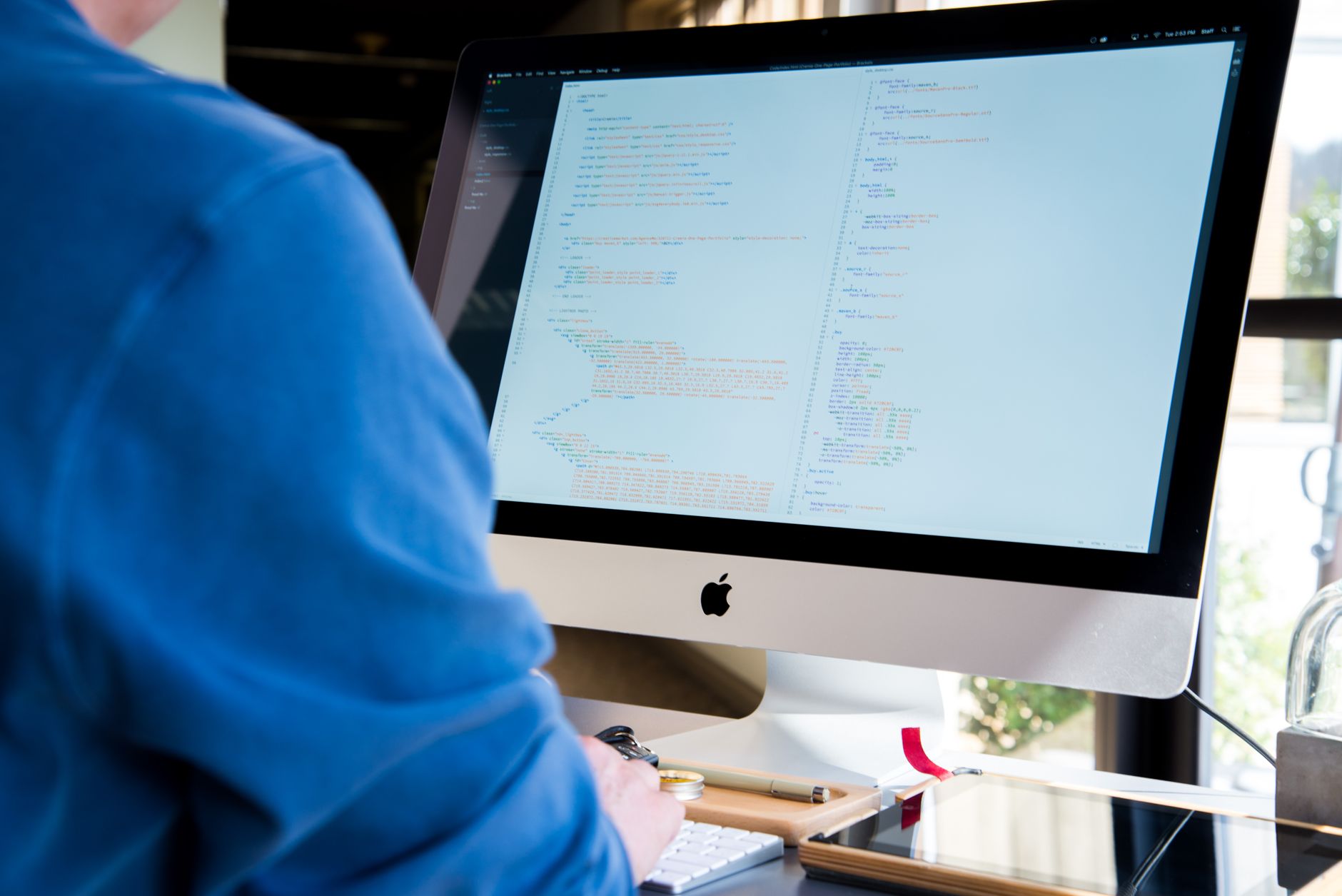 Programista w niebieskiej koszuli kodujący na komputerze iMac